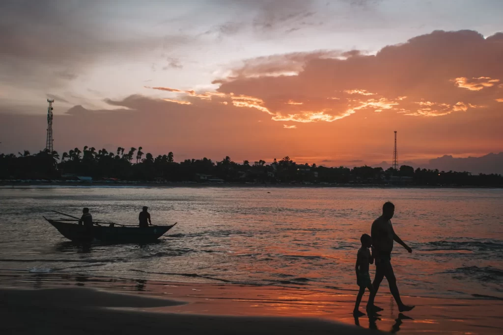 Orange clouds at sunset at Arugam Bay beach with two people walking past a little fishing boat