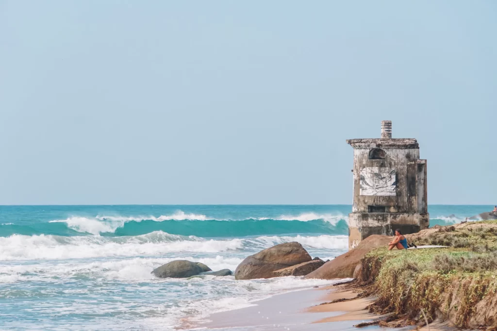 A surfer sits next too the lighthouse watching the waves at lighthouse point break near Arugam Bay