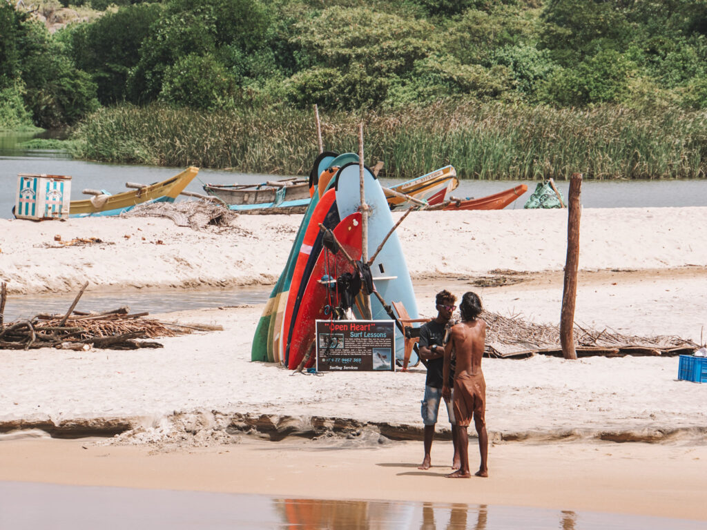 Two local Sri Lankans chatting on the beach next to a surf board rental stand on Elephant Rock beach