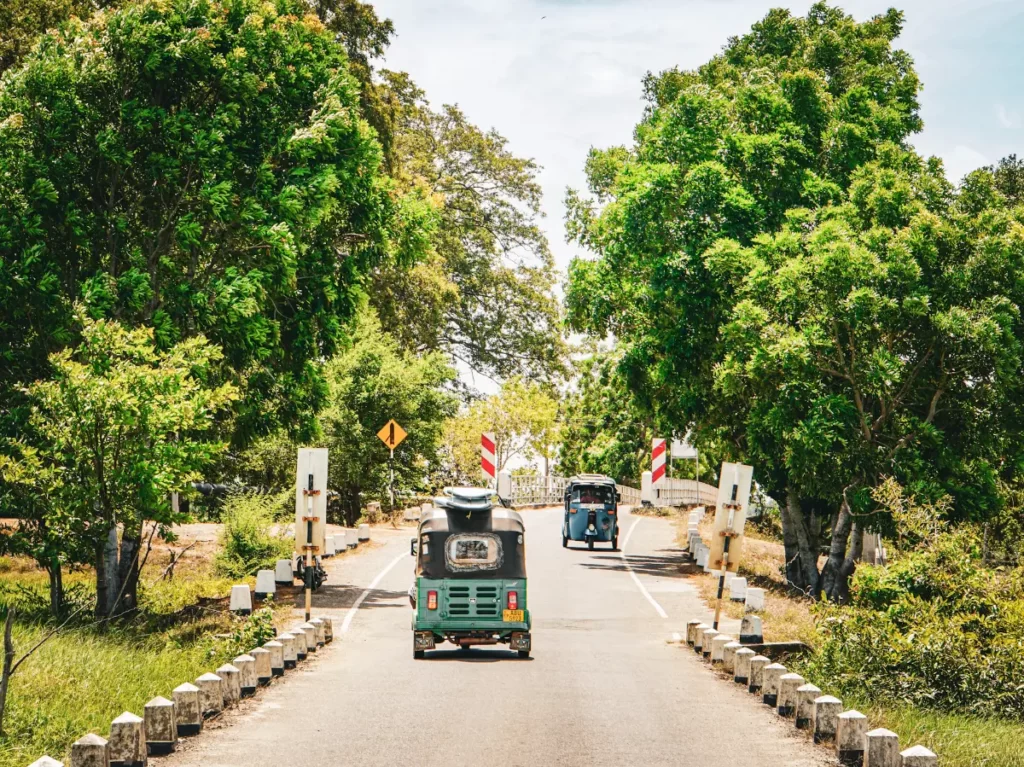 Two Tuk Tuks cross a bridge with surfboards on their roof on the way to Peanut Farm Beach