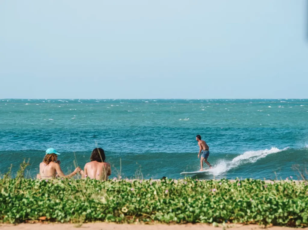 A surfer catches the beach break at Peanut Farm with two people watching