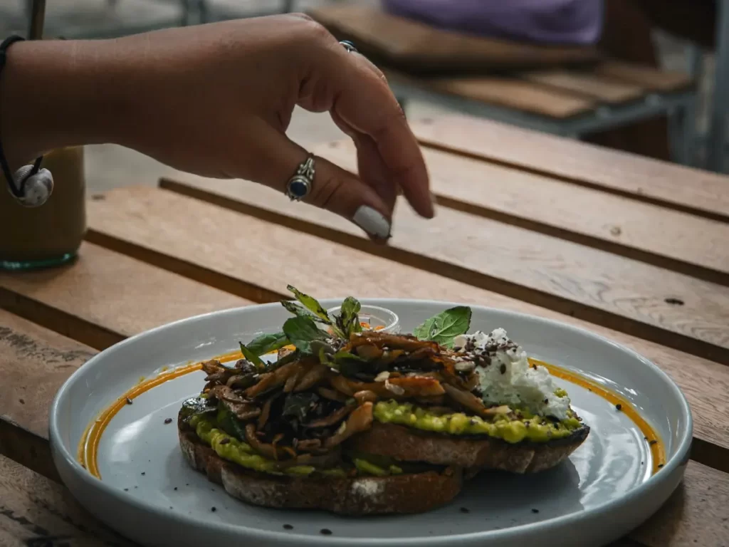 A girl sprinkles pepper on a feta and mushroom avocado toast at Shady Lane in Arugam Bay  
