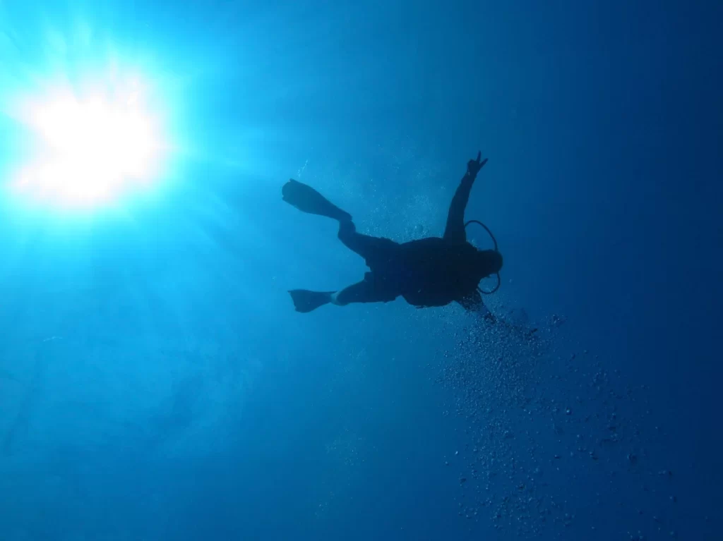 A diver descending from the surface with the sun in the sky at Unawatuna Lord Nelson Shipwreck diving spot