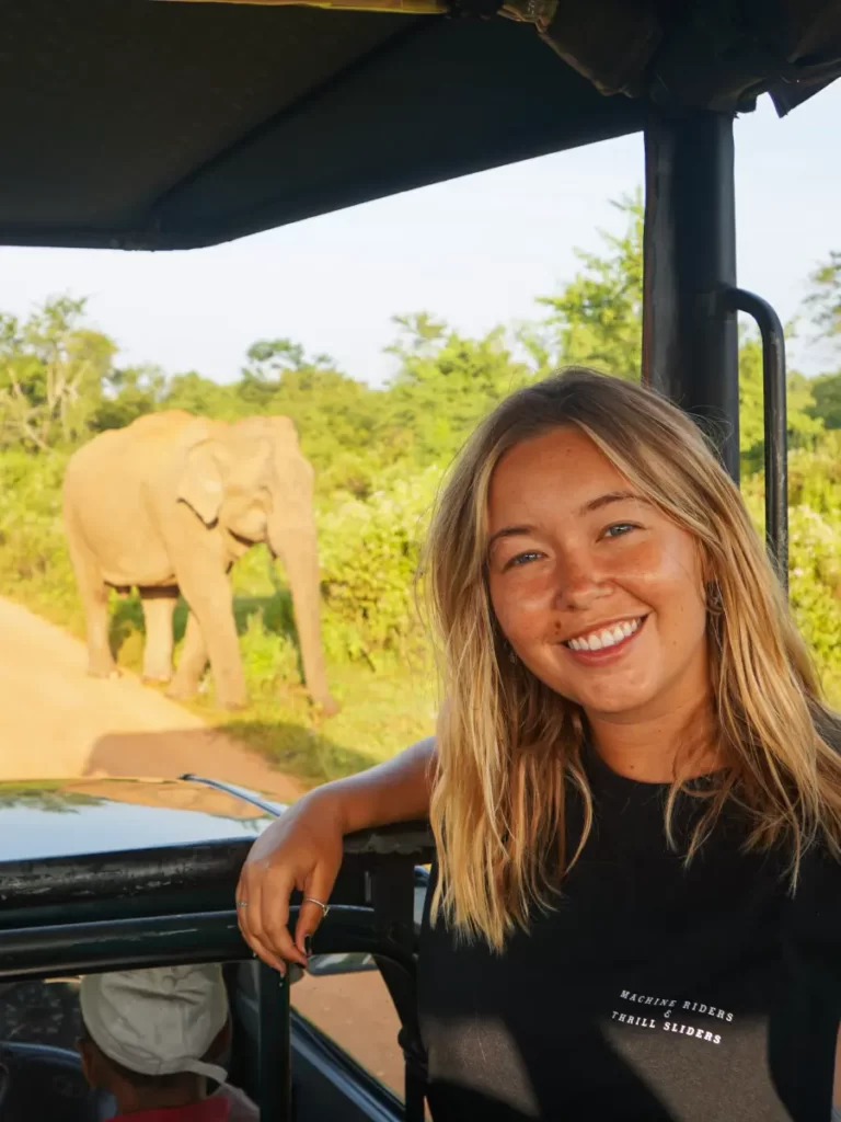 A girl smiling in a jeep with an Elephant in the background