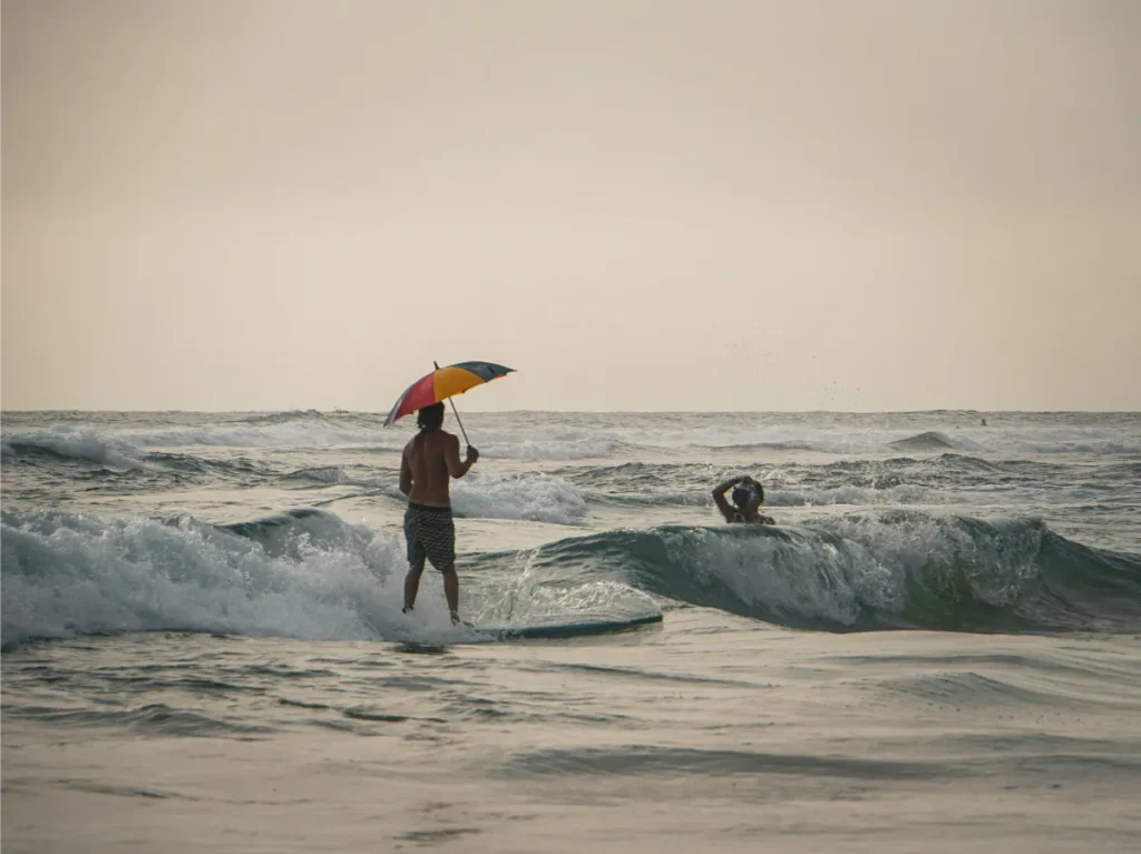 A surfer holding an umbrella on a wave at Ahangama Beach