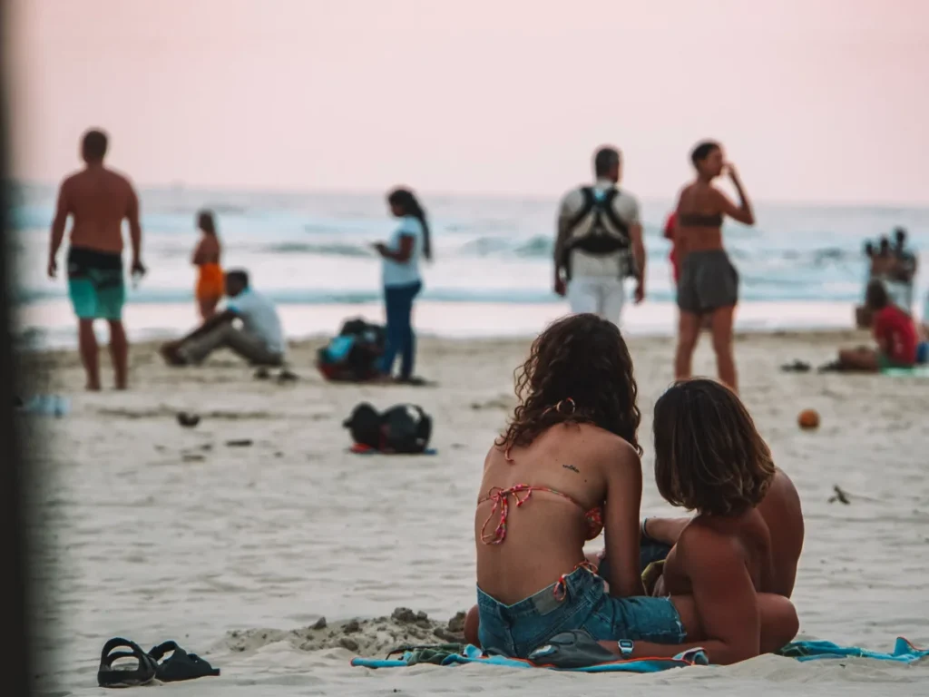 A couple lies on the sand with people hanging out in the background at Kabalana beach