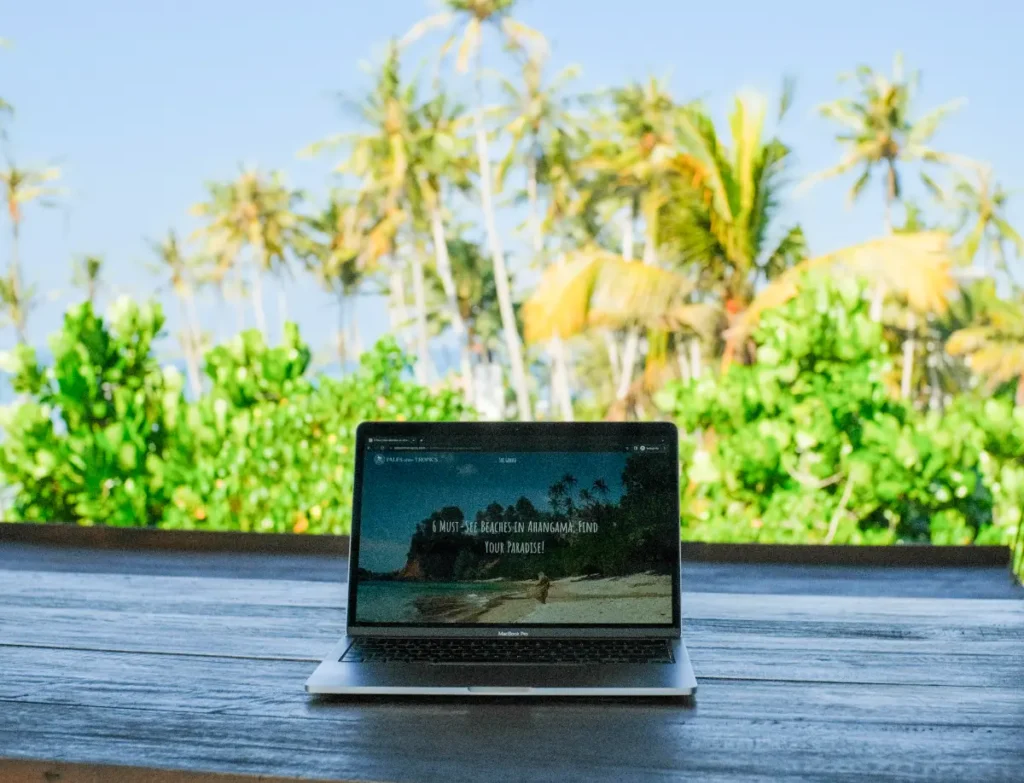 A laptop on a bench and palm trees in the background
