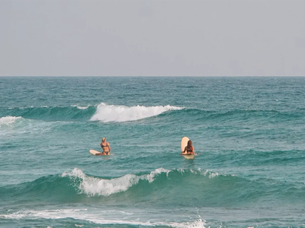 Two surfers sit in the ocean waiting for a wave