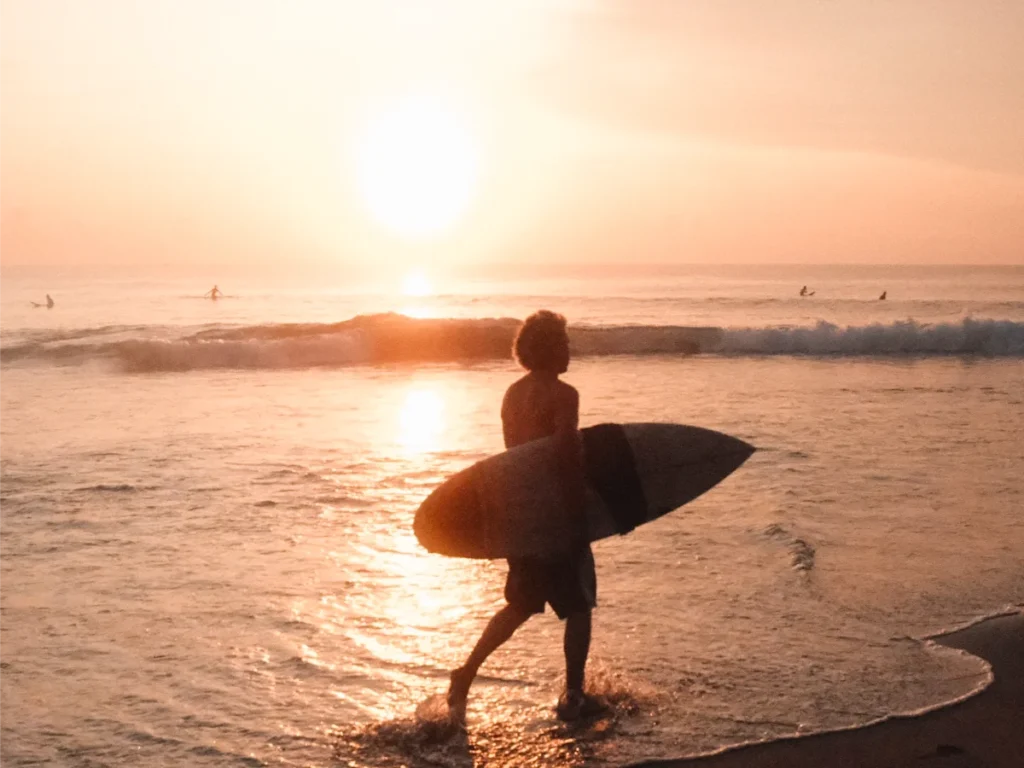 A surfer walks to main point as the sun rises above the horizon