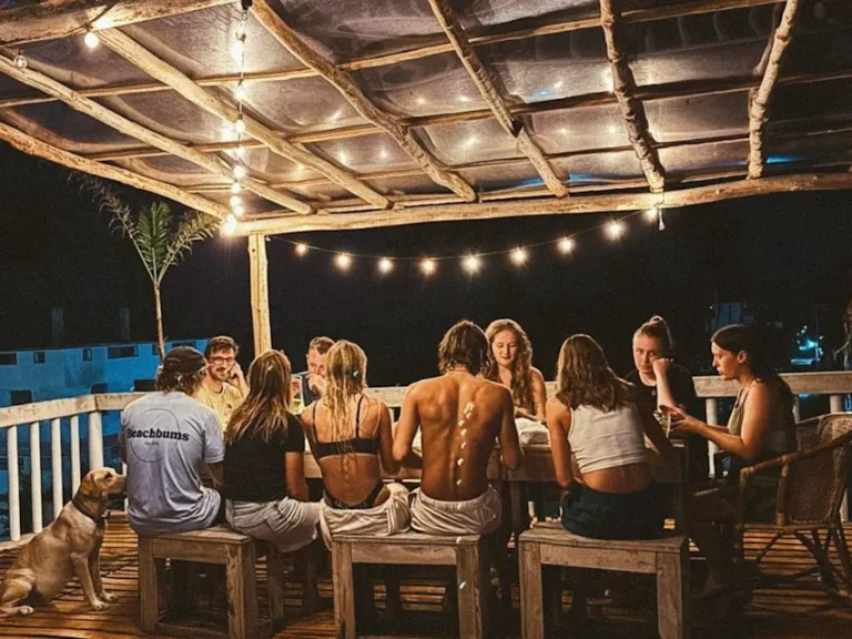 A group of travellers eat a communial dinner on Beachbums coliving rooftop, a top place to stay in Madiha